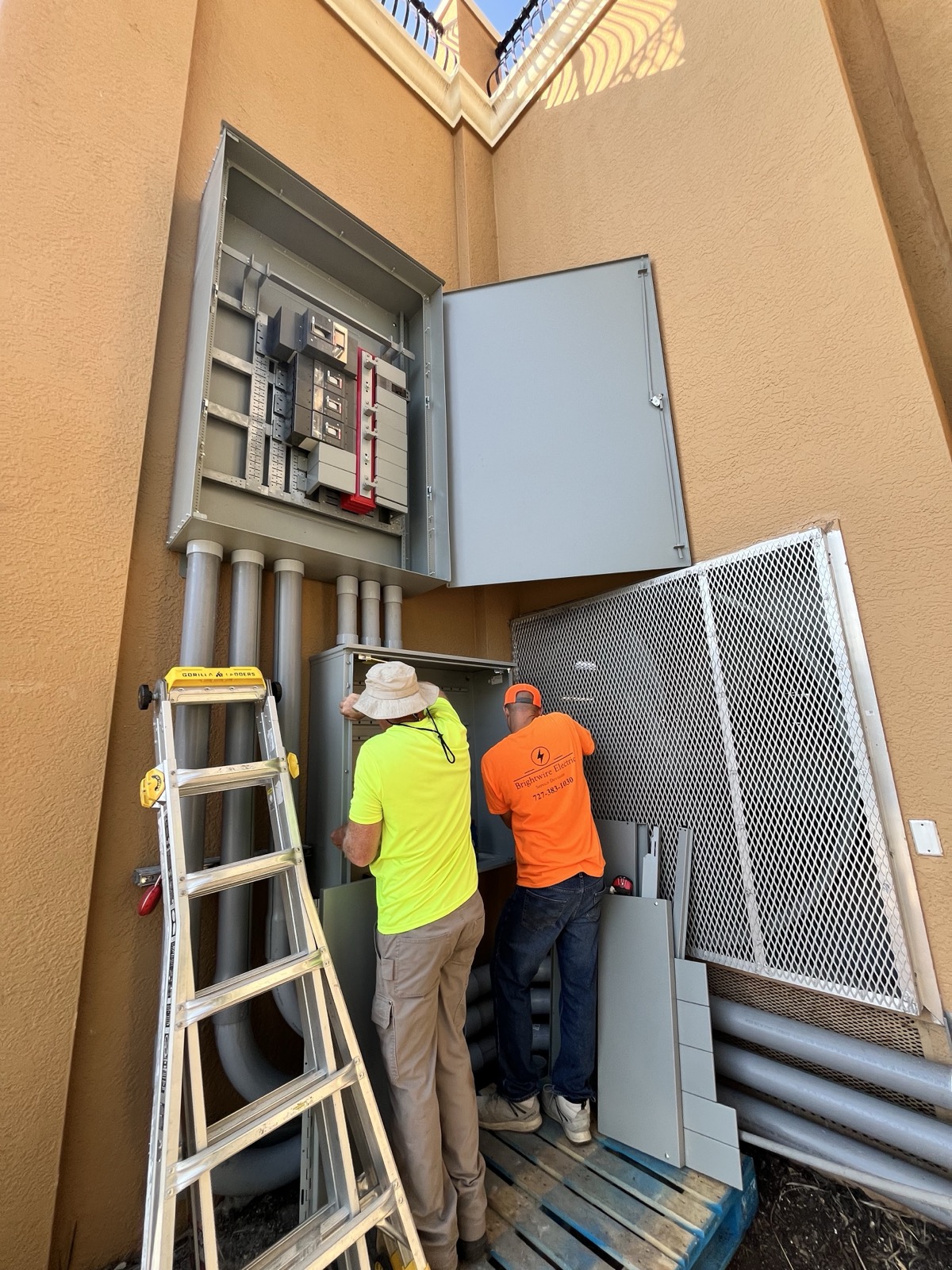 Two workers servicing a large exterior commercial electrical panel for Brightwire Electric